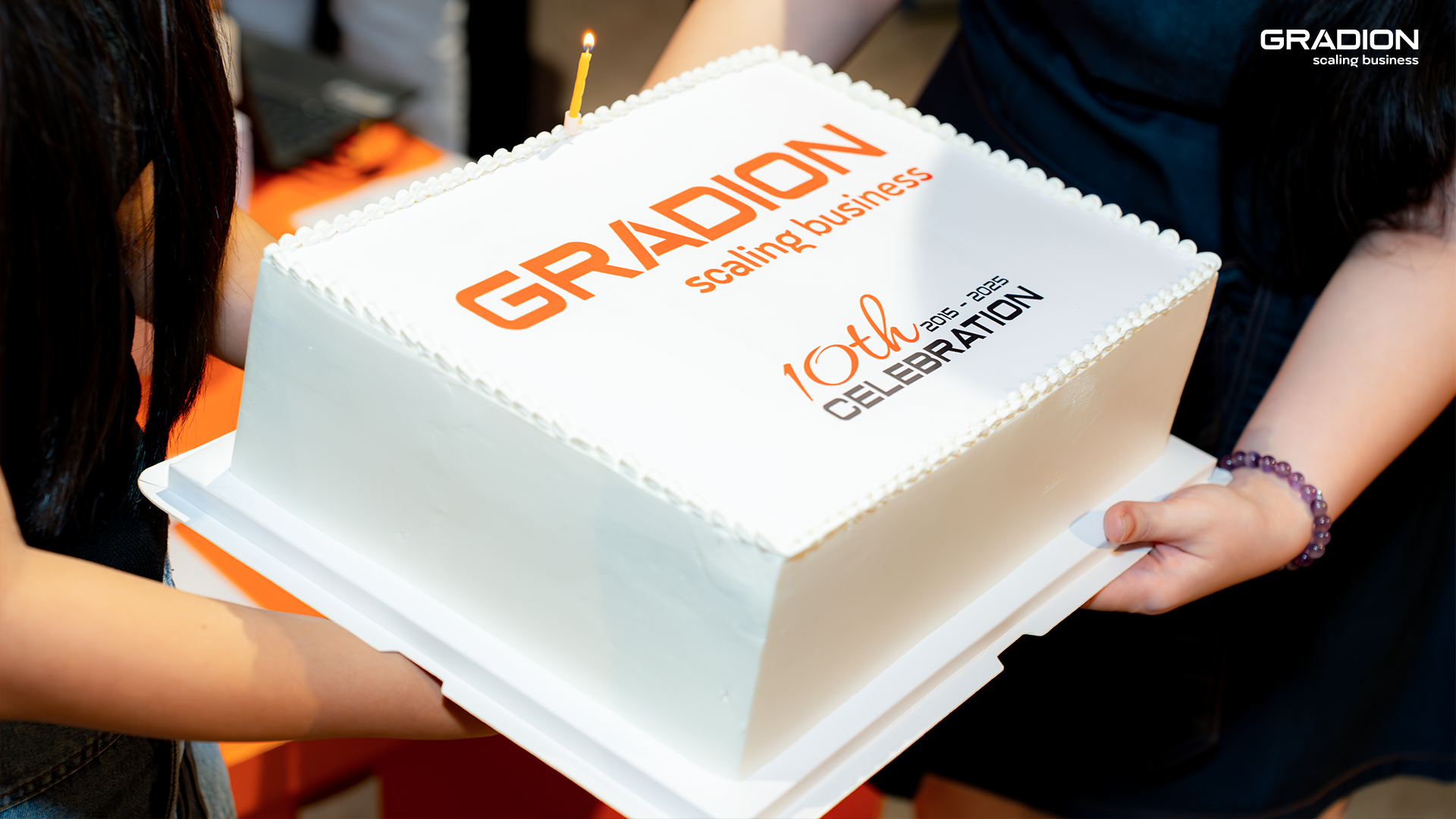 Gradion 10th anniversary celebration cake with company logo and single lit candle, symbolizing a decade of scaling business